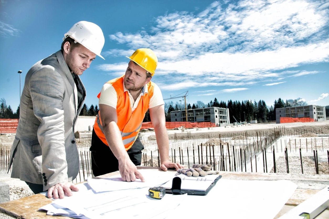 Two men in hard hats and vests looking at plans.