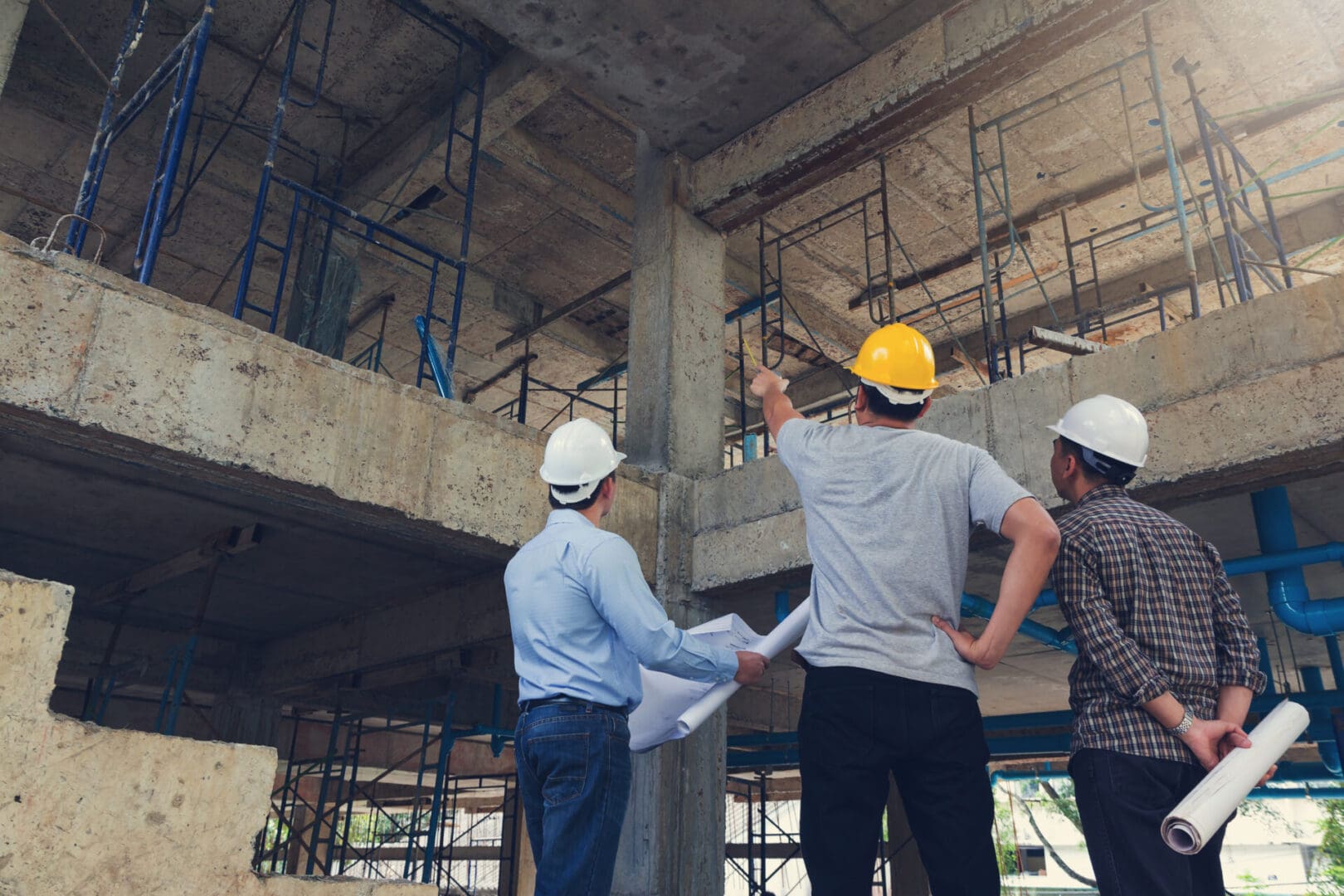 Three men in hard hats are standing on a building site.